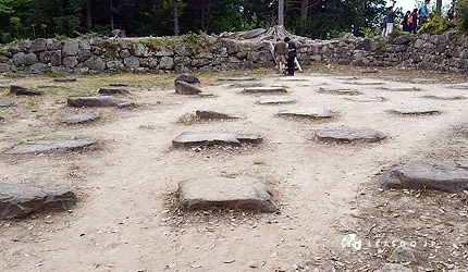 安土城迹山顶天主台遗址,仅剩散落的方形础石排列于平坦土地上,周围为树林