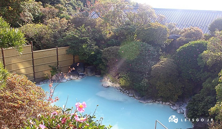 岡本屋旅館戶外露天風呂,藍白色溫泉水池四周環繞綠樹與石牆