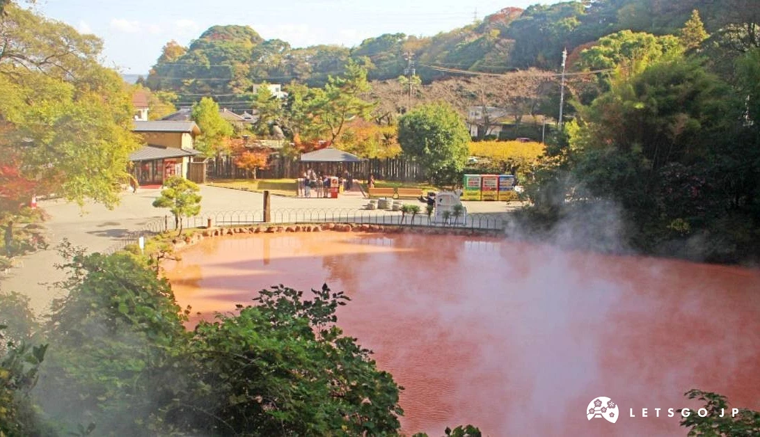 深紅色的溫泉池周圍有綠樹遠方有山