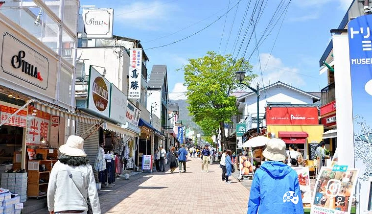 晴天下的旧轻井泽银座通商店街,两旁林立特色店铺与洋风建筑,街道上有许多游客悠闲散步与逛街