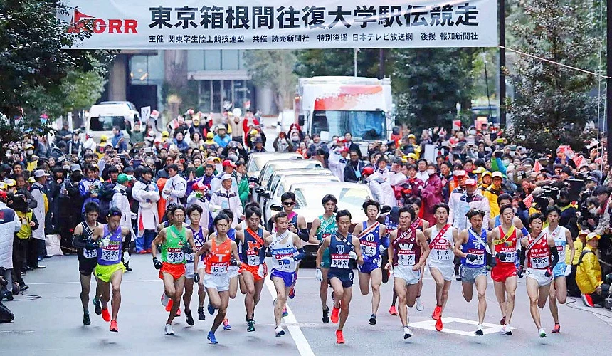 多支大学生队伍在箱根駅伝比赛起点同时起跑,两侧可见大量观众与媒体,展现日本新年期间的热门运动赛事景象