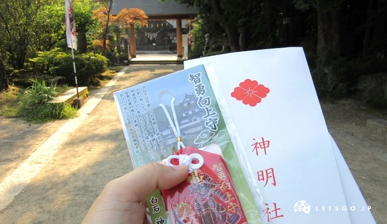 神明社參道兩側樹木茂密,手持神明社御守與繪馬