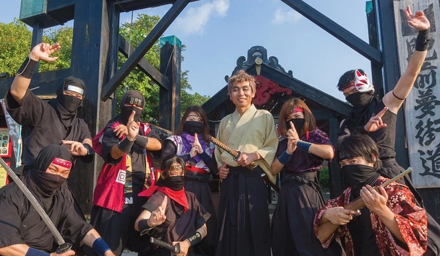 一群身穿忍者服的演员围在中间持刀男子,背景有古风街道入口木架