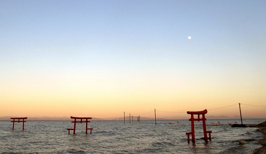 夕暮时分,湖边水中散落多座朱红色鸟居,远处的湖面与山脉轮廓映衬在淡紫色天空上