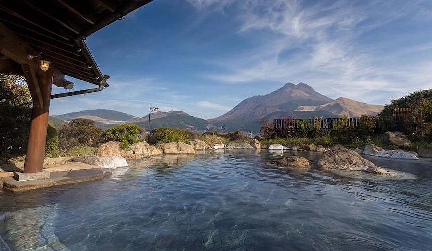 大分縣別府市,夕陽下溫泉蒸氣繚繞的城市景觀,有遠方山巒為背景