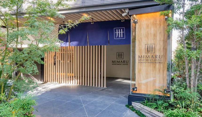 MIMARU 飯店入口採木格柵與藍色布幔設計,周圍綠意盎然,營造出兼具日式傳統與現代感的溫馨迎賓氛圍