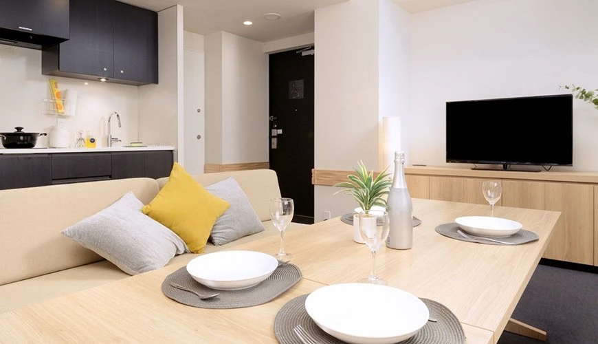 MIMARU 大阪飯店房內配置齊全,可見開放式廚房、餐桌、沙發與電視,整體採溫暖木質調設計,呈現寬敞舒適的公寓式空間