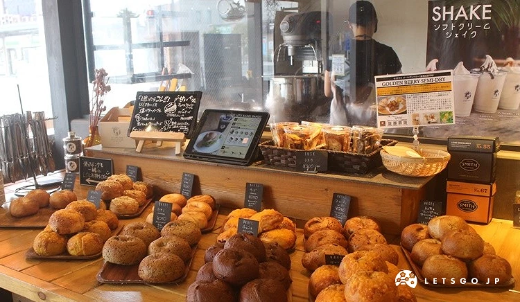 「Lit work place」的餐檯展示,擺放著大量的圓形貝果和麵包,上方有飲料和餐點的菜單看板。