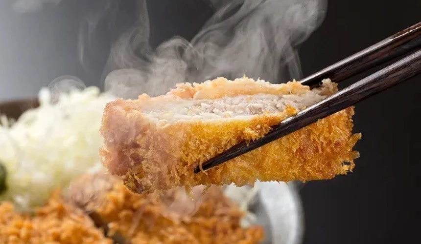 一雙黑色筷子夾起一塊熱騰騰的炸豬排
