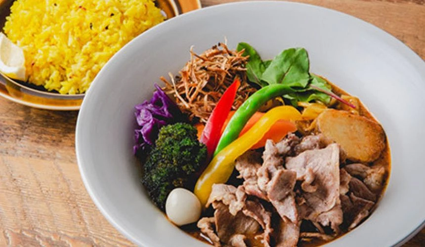 盛装于白色碗中的札幌汤咖哩料理,配有多种蔬菜与肉片,旁边摆放姜黄饭,呈现丰富又诱人的北海道风味