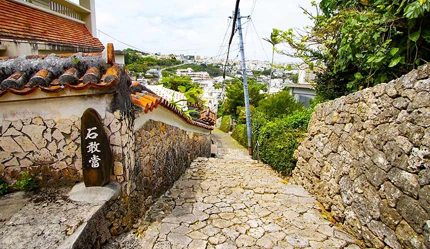 金城町石叠道街景,石板坡道两侧为琉球石墙与红瓦屋顶建筑,可远望那霸市区景色