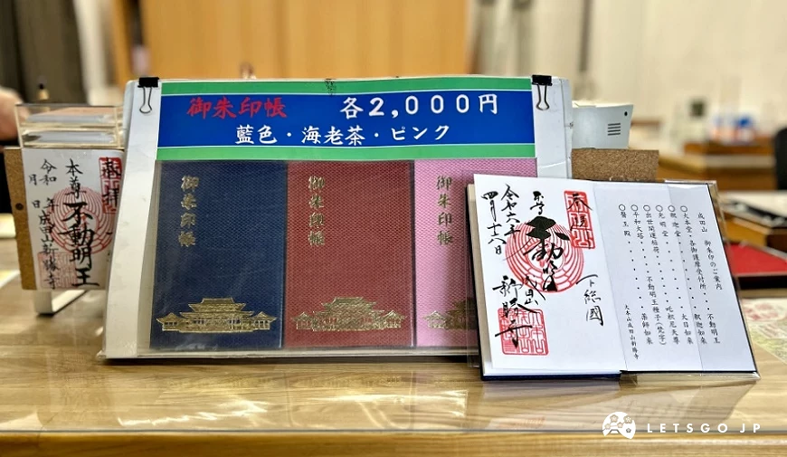 成田山新勝寺御朱印帳與御朱印展示,櫃台上可見多款不同顏色的御朱印帳與蓋有紅色印章的御朱印紙