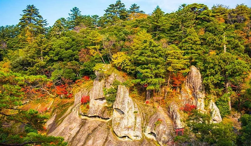 石川县小松市那谷寺秋季景观,奇岩峭壁与红叶交织,山门与步道隐现其中,展现日本古刹的幽玄之美