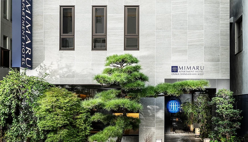 MIMARU大阪 心齋橋WEST 飯店外觀以灰白色牆面與綠色松樹景觀為主