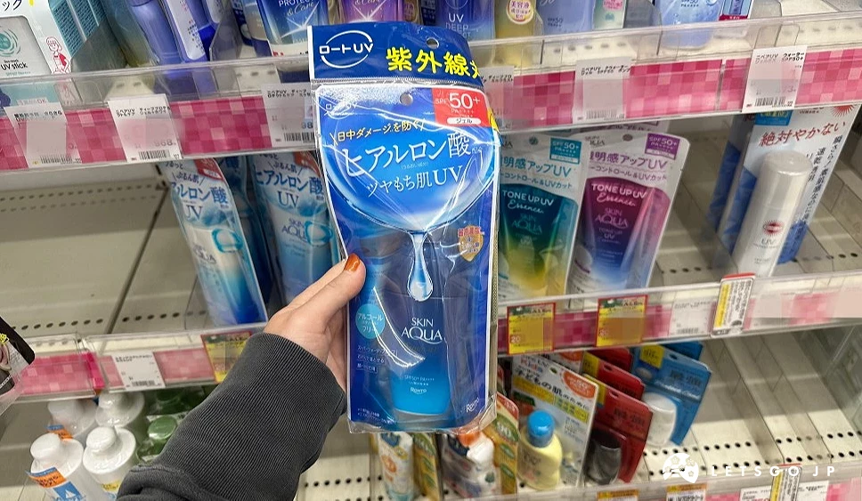 一位女性的手拿着蓝色包装塑胶袋上面印有日文字样的防晒精华站在商品架前