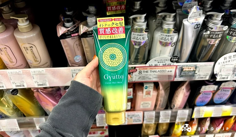 一位女性的手拿着一条绿黄色渐层上面印有英文Gyutto的挤压式条状商品站在商品架前