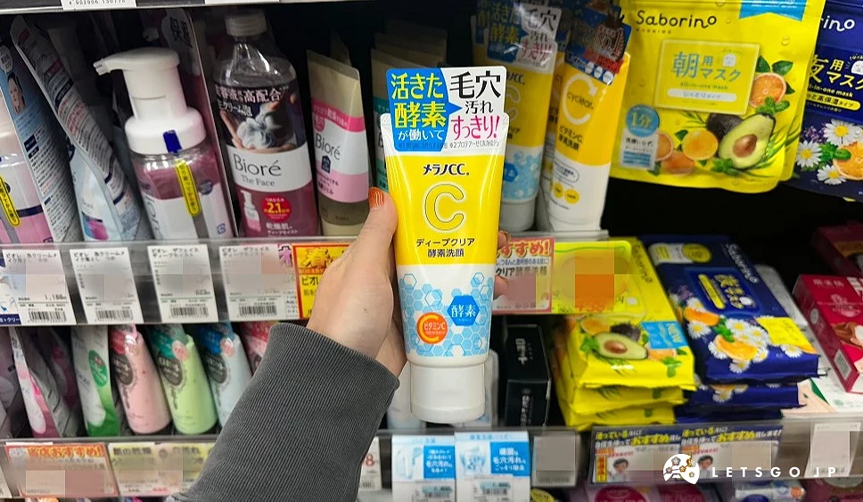 一位女性的手拿着一条黄白相间上面印有日文并有一个英文字母C在瓶身的挤压式条状商品站在商品架前