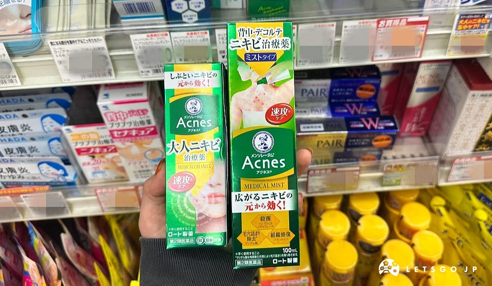 一位女性的手拿着两条绿色上面印有英文Acnes的长方形纸盒商品站在商品架前