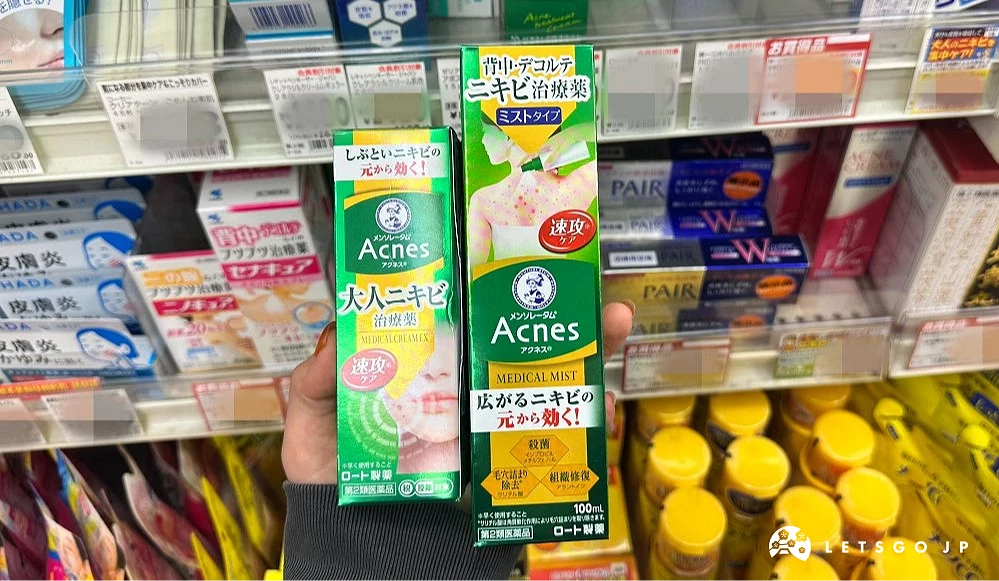 一位女性的手拿着两条绿色上面印有英文Acnes的长方形纸盒商品站在商品架前