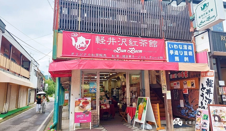 位于旧轻井泽银座通商店街的轻井泽红茶馆 (Sun Beam) 店面,鲜红色的招牌与遮雨棚非常夺目,门口摆放着精致的下午茶推荐海报,店内专卖各式原创红茶与茶包组合