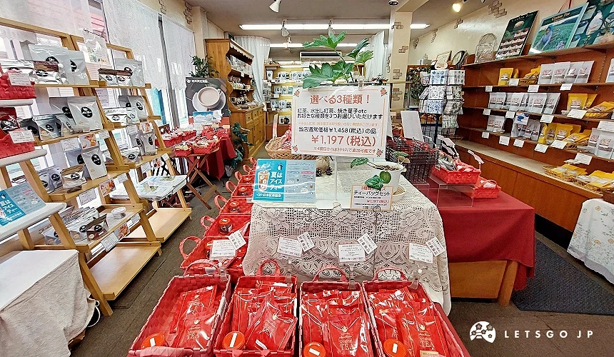 轻井泽红茶馆 (Sun Beam) 的店内环境,桌上整齐摆放着红色的茶包礼篮,上方设有「任选 3 种类」的优惠海报,价格标示为 1,197 日元(含税)。墙边货架陈列着各式原创红茶与精致茶具组合。