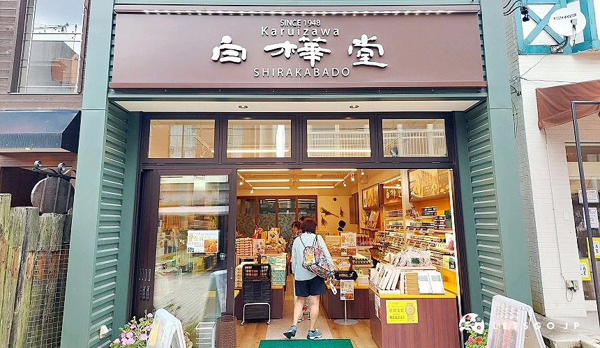 位于轻井泽的白桦堂 (SHIRAKABADO) 店面,深棕色招牌配上白色的品牌字体,门口展示着获得金赏肯定的伴手礼海报,店内陈列着各式知名点心与甜点