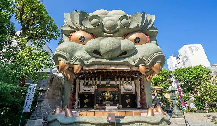 難波八阪神社的獅子殿外觀,巨大的獅子頭正張開大口,綠色外牆與誇張表情十分醒目,前方為參道與樹木