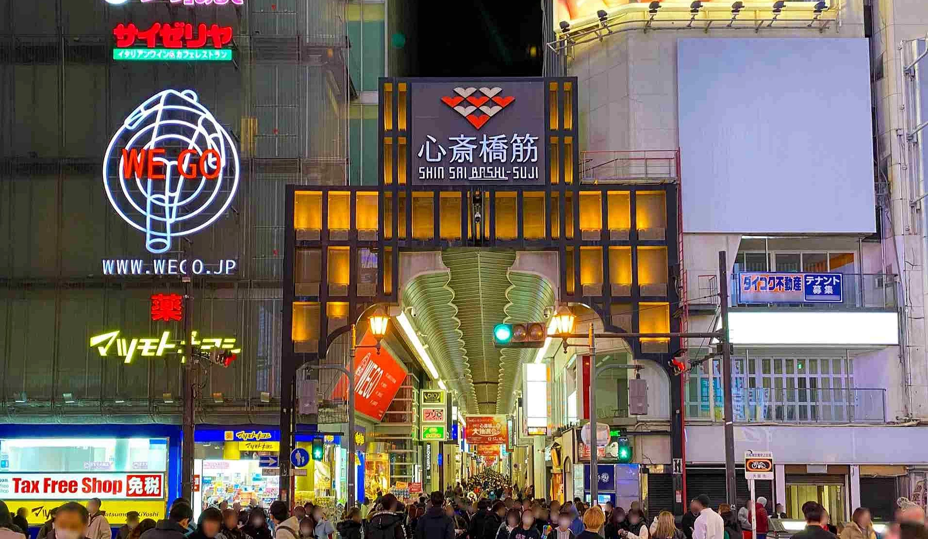 心斋桥筋商店街入口夜景,招牌灯光亮起、街道两侧店铺林立,吸引大量人潮进入逛街购物。