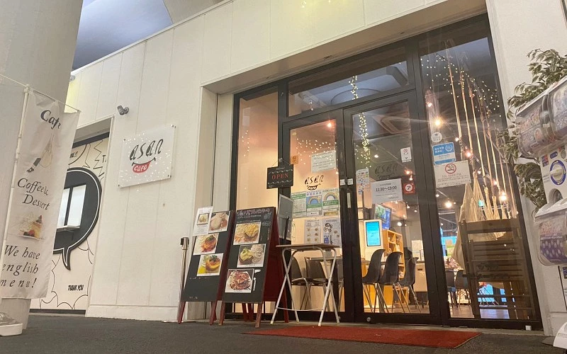 玻璃門店面，牆上有英文字樣，門口擺放看板，內部有桌椅和燈飾