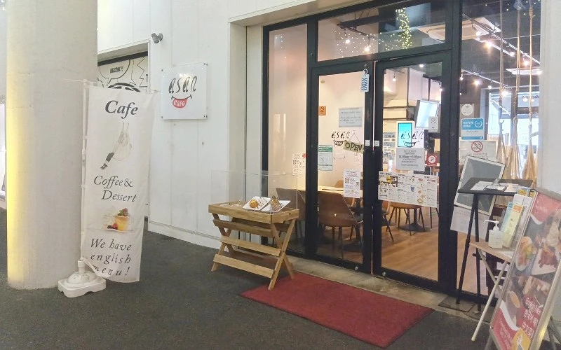 白色牆面店鋪有玻璃門，門口擺放木桌和紅色地毯