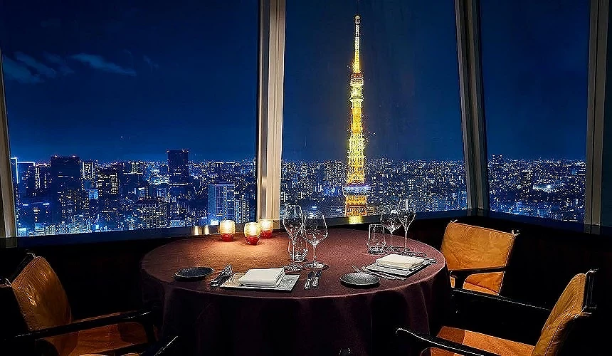 東京鐵塔夜景景觀餐廳窗邊圓桌,餐桌擺設精緻,窗外可見燈光閃耀的東京鐵塔與城市夜景,營造浪漫用餐氛圍。