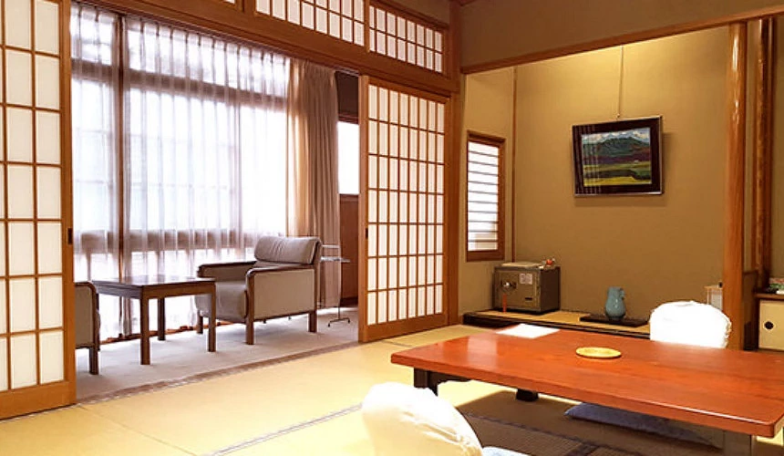 月本屋旅馆客房内叠叠米上有木头方形桌子及可靠背椅垫约有6至14帖大小