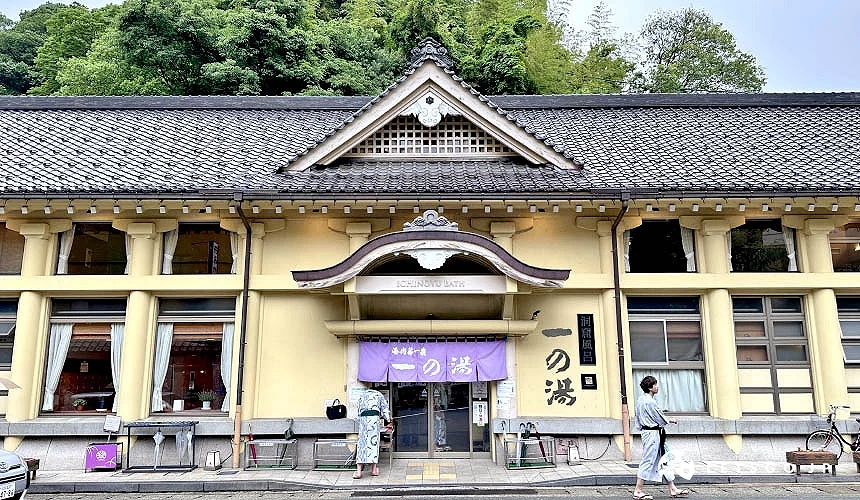 一栋鹅黄色墙壁的建筑物有着紫色暖帘上写着一之汤的城崎温泉七大外汤一之汤外观