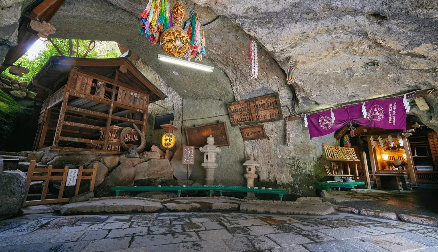石窟內有木造小神社、石燈籠,岩頂懸掛彩色千羽鶴和裝飾,右側有紫色幕簾