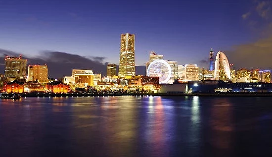 夜間拍攝的圖片,前面是海面,後方是多棟開著燈光的大樓和摩天輪