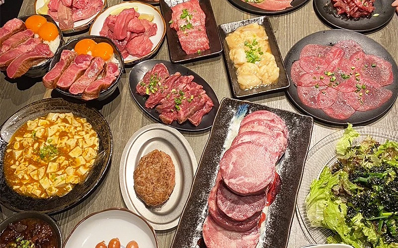 桌上滿滿擺放各式燒肉盤和料理，有生肉、雞蛋和蔬菜