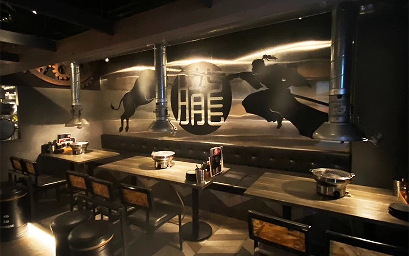 燒肉店內部有牛隻剪影壁畫，前方擺放餐桌和燒烤設備