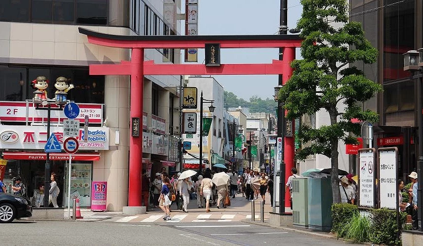 紅色鳥居下面有行人在行走,通過鳥居是一條商店街。