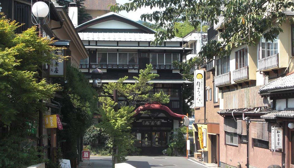 窄道盡頭有一棟木造樓房,入口覆紅色屋頂,左右並列傳統旅館與招牌,路旁交錯樹木