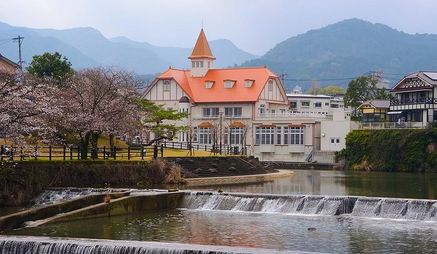 河畔橘色屋顶的温泉建筑前方,小瀑布流过,樱花点缀河岸