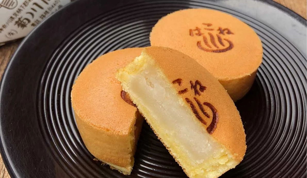 黑色圓盤上擺放兩枚圓形糕點,其中一枚剖半裡面有白色餡料,表面烙有日文字樣