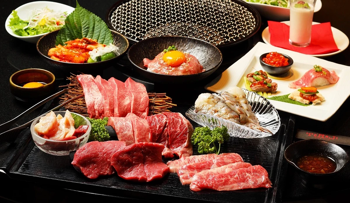 桌上擺放著多盤燒肉用生肉與海鮮,包括肉片、蝦、小碗醬料,旁邊有沙拉與飲品。