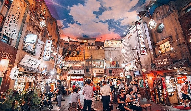 模擬昭和時代街景的市內空間,屋頂上畫有藍天和白雲,街道有多家商店,周圍有燈光和人群走動。