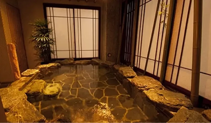 充满日式氛围的室内温泉浴池,周围铺设自然石材,搭配竹帘与和纸拉门,营造静谧放松的泡汤空间