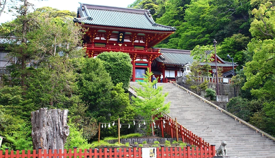 前面有紅色欄杆,右側有岩石階梯,階梯上去有一棟紅色建築,左右兩側有綠色樹林