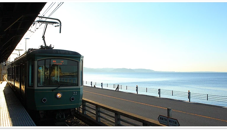 左側是綠色的電車,右邊有馬路,馬路外側是一片海