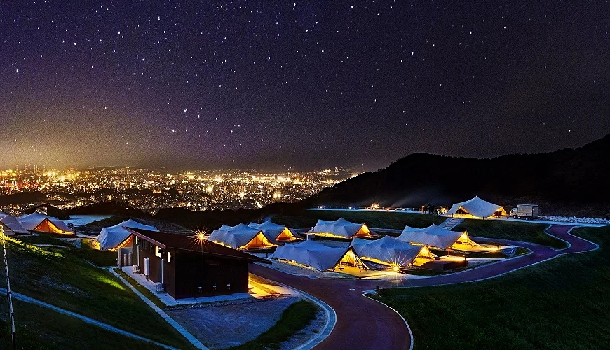 山坡上整齊帳篷群夜景,遠處城市燈火與滿天星空