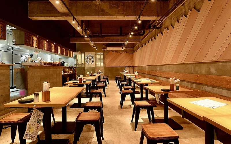 店內整齊排列木桌椅，後方可見廚房與開放式吧檯