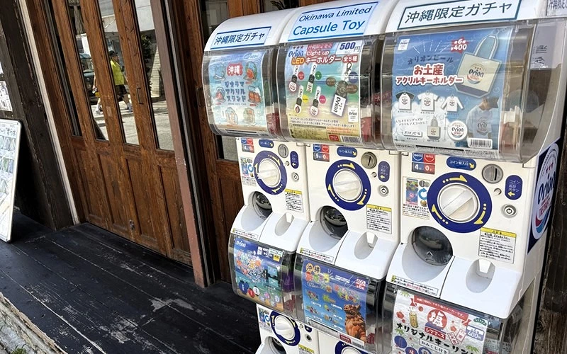 木門前擺放多台扭蛋機，上方標示「沖繩限定ガチャ」