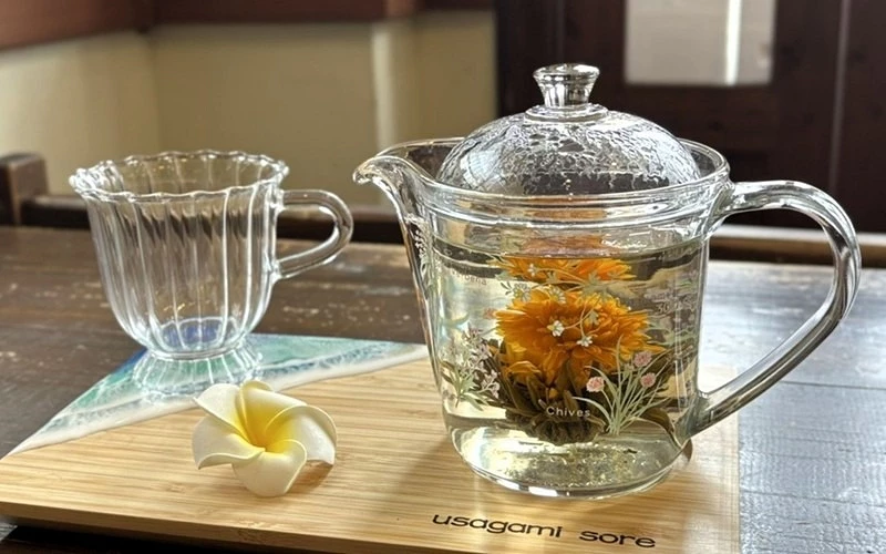 透明玻璃壺中沖泡著橘色花茶，旁邊放有玻璃杯與白色雞蛋花